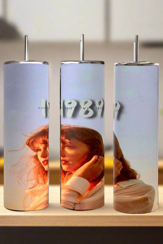 Three Kreative Kreationz Taylors Version 1989 20oz Tumblers with straws are displayed on wood. Each eco-friendly stainless steel tumbler shows a woman with red hair in sunlight, and 