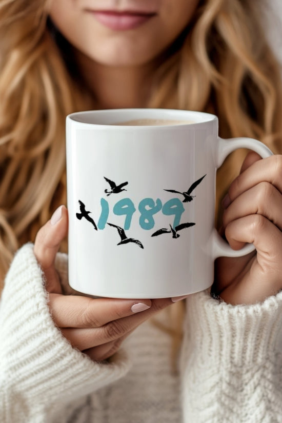 A woman with long, wavy blonde hair holds a Kreative Kreationz 1989 Ceramic Mug, featuring 