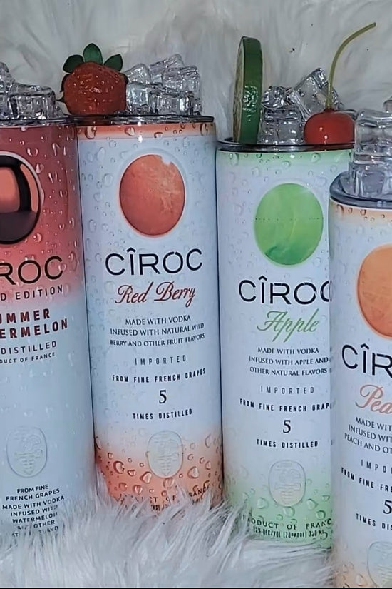 Two cans of Kreative Kreationz Ciroc 20oz Tumbler with 3D Lid Topper are shown on a wooden surface, reminiscent of travel tumblers. The left can is Red Berry flavor, topped with ice and a cherry. The right can is Vodka Snap Frost flavor, topped with ice and a lemon slice. Both cans feature product information and branding.
