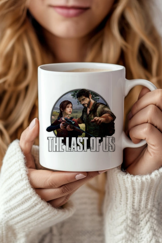 A woman in a white sweater holds the Kreative Kreationz The Last Of Us Ceramic Mug, featuring game characters in a striking photographic design with the title printed below.