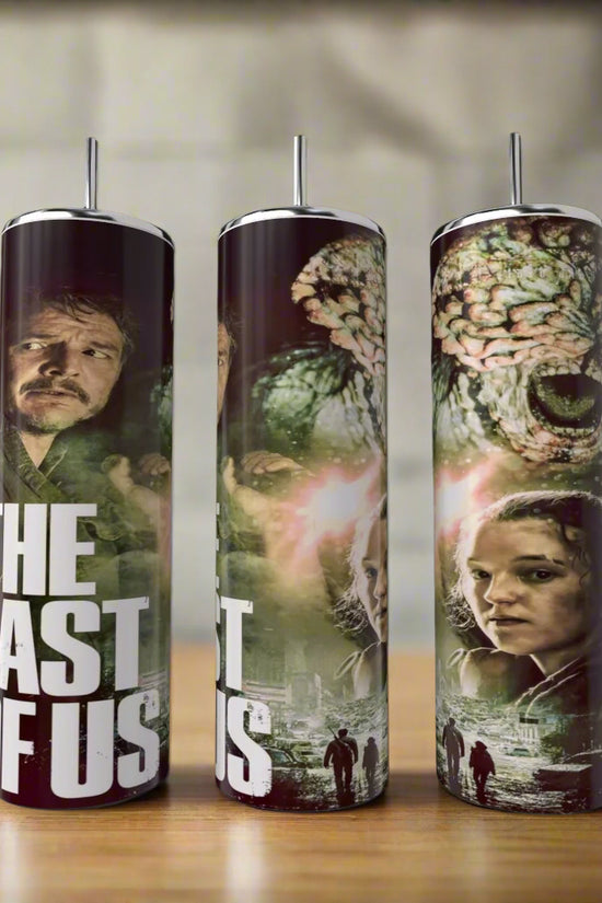 Three tall The Last Of Us Tumblers by Kreative Kreationz, featuring main characters, post-apocalyptic scenes, and a monstrous creature sit on a wooden surface—perfect eco-friendly drinkware for fans of the series.